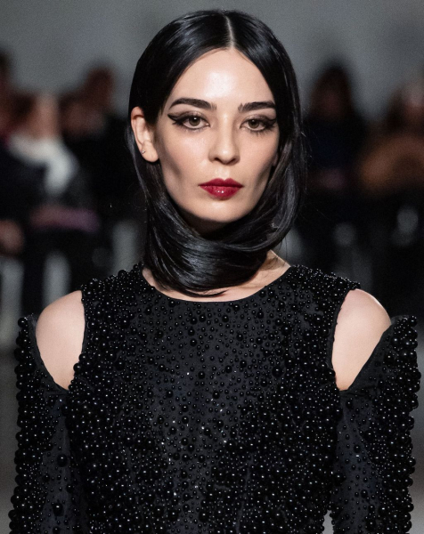 A model wears her dark hair wrapped around her neck and a beading black dress